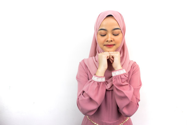 美丽的微笑的亚洲妇女在粉红色头巾保持手在下巴下，闭上眼睛，孤立的背景图片下载