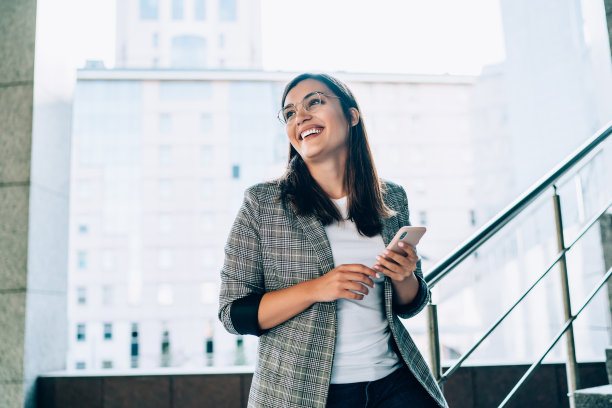 快乐的白人潮女孩笑着在手机上得到有趣的信息站在城市背景上，微笑着美丽的千禧漂亮女人满意的智能手机上的银行应用程序图片下载