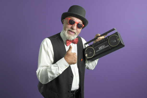 伟大的80年代。一位穿着老式经典套装的老人，紫色背景上放着一台盒式录音机。图片下载