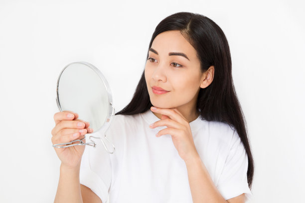 年轻的亚洲女子看着镜子孤立的白色背景。副本的空间。护肤和抗衰老的胶原蛋白概念。宏观完美的韩国女孩脸。图片下载