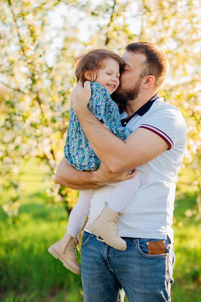 在春天盛开的花园里散步时，爸爸又拥抱又亲吻他的小女儿。图片下载