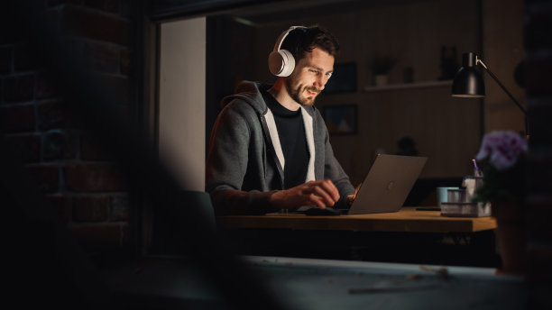 快乐的软件开发人员在笔记本电脑上工作。开朗的信息技术专家，戴着耳机，听音乐，做专业的工作。在家办公的远程工作概念。图片下载