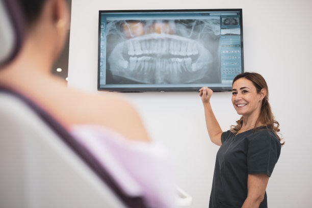 医学、牙科和保健概念——女牙医在牙科诊所向病人展示电视上的牙齿x光片。图片下载