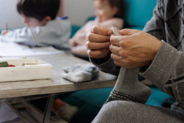 孩子们做作业的时候，一个男人在家里的客厅缝袜子图片下载