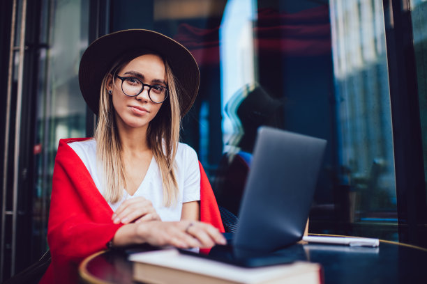 内容潮女人在帽子使用笔记本电脑和坐在桌子在寒冷的咖啡馆露台图片下载