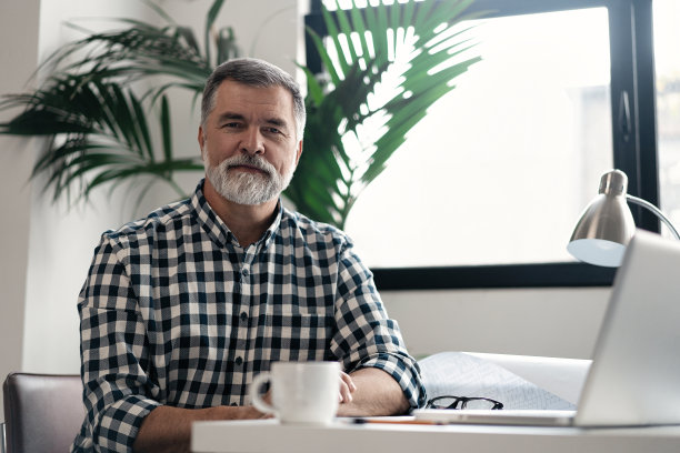 成熟自信，面带微笑的建筑师，穿着休闲装，在现代明亮的办公室里与蓝图文件和图纸一起工作。图片下载