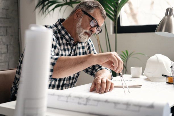 成熟的建筑师在现代化的办公室工作蓝图。工程师在图纸上使用分隔罗盘工具图片下载