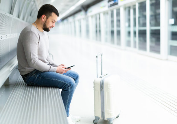 留着胡子的旅客拿着手机在地铁站的长椅上等火车图片下载