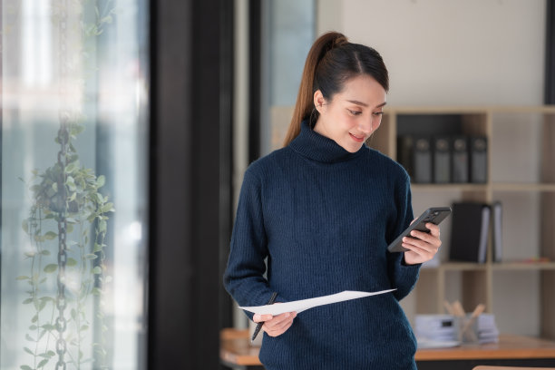 亚洲女商人拿着文件报告，在办公室工作时使用手机的图片图片下载