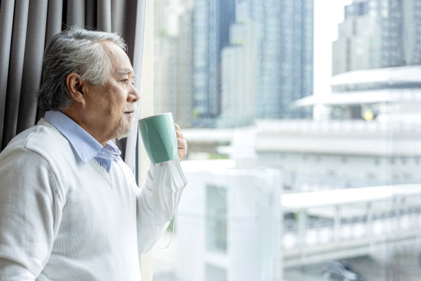 亚洲老年退休老人站着手拿着热饮看着窗外家的隔离概念，老人等待封锁是家内部的背景图片下载