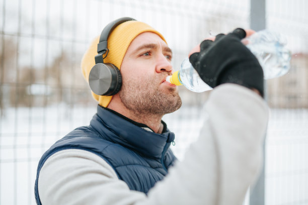 冬日补水作为一个坚定的跑步者，他戴着耳机，正在快速休息以补充水分图片下载