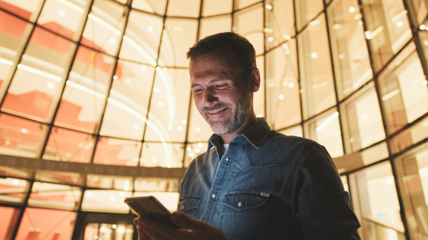 特写，中年男子晚上站在商业中心旁边使用手机图片下载