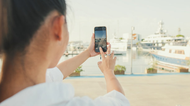 年轻女子用手机拍下海港的照片。后视图图片下载