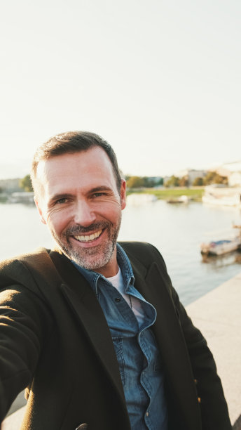 近景，一名男子在河堤上用手机进行视频通话。背光图片下载