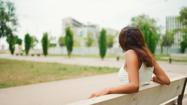 可爱的黝黑的女人，棕色的长发，穿着白色的上衣，坐在公园的长椅上放松地看着别处。生活方式概念。缓慢的运动。图片下载