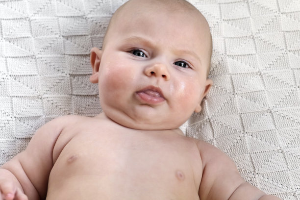 白色针织毛毯上的美丽婴儿肖像。头和脸。孩子的脸颊涂满了奶油。新生儿躺着，看着摄像机。母亲、健康、儿科。可爱的小婴儿。特写镜头图片下载