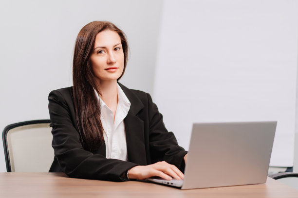 深色头发的女人，穿黑色外套，办公室里有会议板，台式电脑和笔记本电脑图片下载