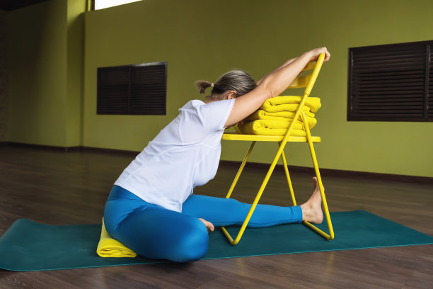 一位生活方式健康的女性正在做瑜伽，她在健身中心穿着运动服，坐在椅子上进行Janu shirshasana练习，她的头弯到膝盖上图片下载