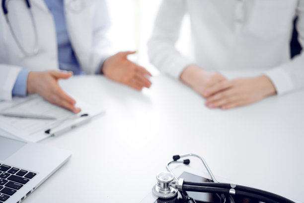 听诊器放在平板电脑上，医生和病人坐在一起。医学、保健概念图片下载