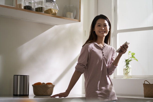 年轻的亚洲女子在家里的厨房里使用手机图片下载