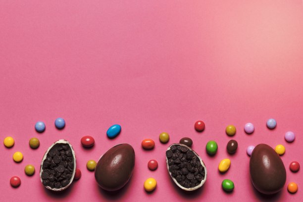宝石糖果巧克力复活节彩蛋充满巧克力片粉红色的背景。高品质美丽的照片概念图片下载