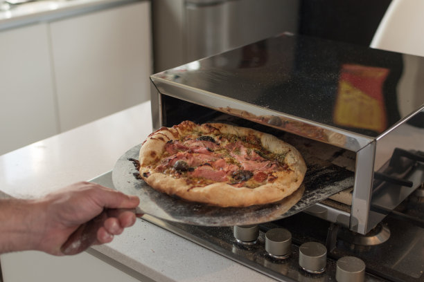 特写镜头:一名男性厨师将烤好的披萨从烤箱中取出图片下载