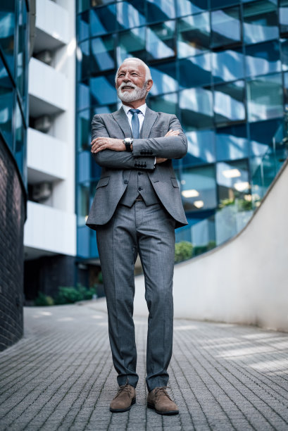 满脸笑容的商人在办公楼外的人行道上双手交叉站着看向别处图片下载