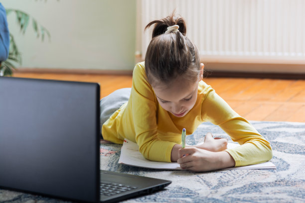 女孩躺在客厅的地板上，用笔记本电脑和书做作业图片下载