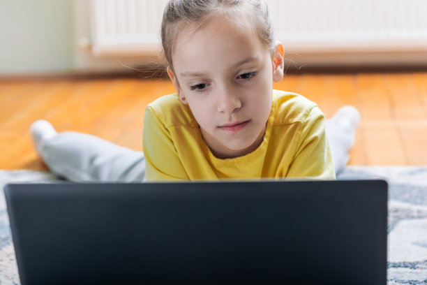 可爱的女孩躺在家里的地毯上，看着笔记本电脑图片下载