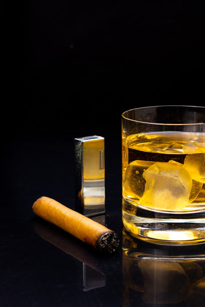 一杯威士忌和一支雪茄在黑色背景上的垂直镜头图片下载