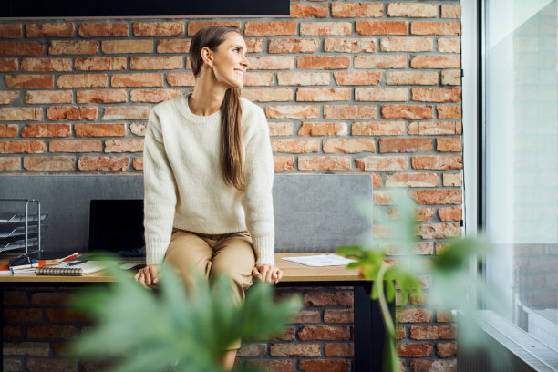微笑的年轻女商人坐在办公室的桌子上透过窗户看的照片图片下载