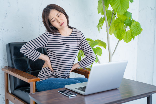 一位在客厅用电脑工作时背痛的女士。图片下载