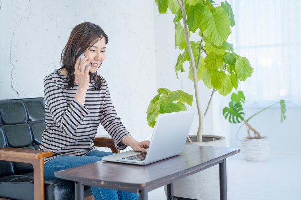 一个女人坐在明亮的客厅里的沙发上，用智能手机聊天。图片下载