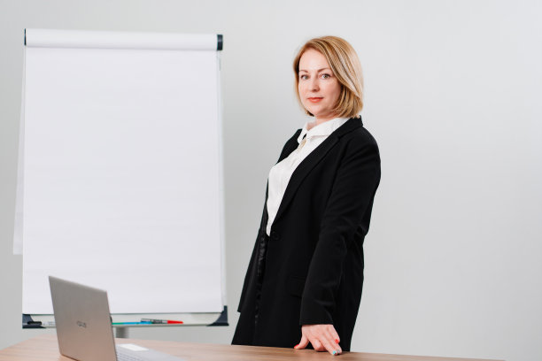 办公室里有个穿黑色外套的女人，手里拿着一块会议板、台式电脑和笔记本电脑图片下载