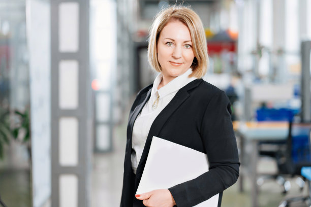 一个穿着白衬衫和黑外套的女人在一个大办公室里。图片下载