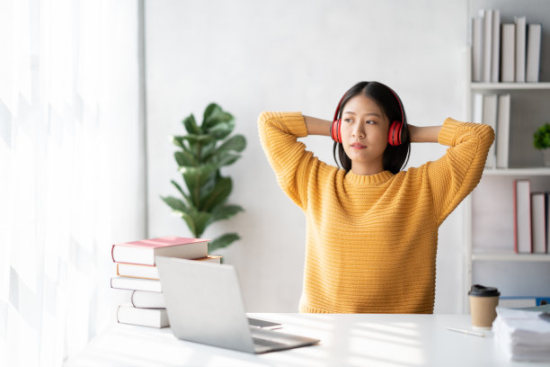 年轻的亚洲女子听着音乐，享受自己努力工作后的学校项目。图片下载