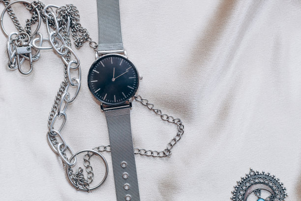 时尚的银链装饰颈部和手表在丝绸光泽的背景图片下载
