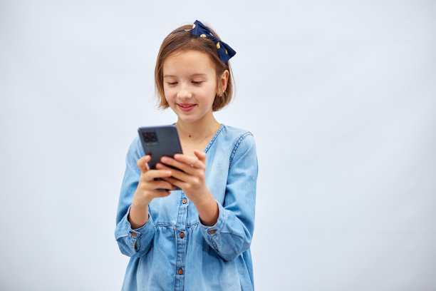 微笑的小女孩在休闲牛仔裙拿着智能手机图片下载