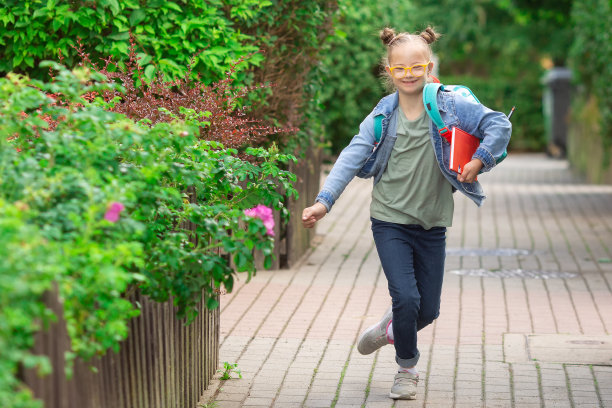 一个患有唐氏综合症的女孩背着书包和书兴高采烈地跑去上学图片下载