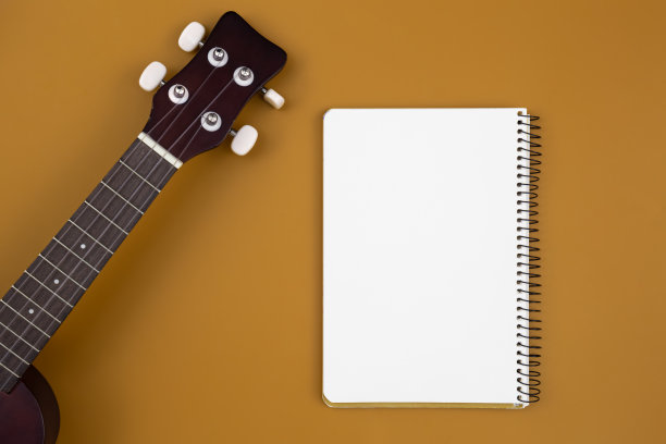 尤克里里吉他和笔记本在棕色背景，平躺。图片下载
