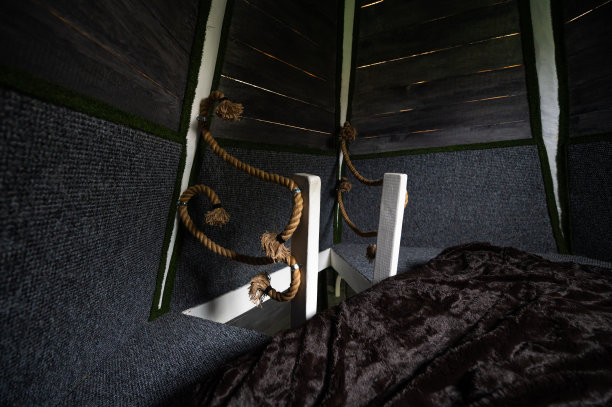 弧形编织麻绳作为木制避暑别墅二楼卧室楼梯栏杆框架的装饰和安全元素。连接到木条的绳子的末端刷。平房二楼的床。图片下载