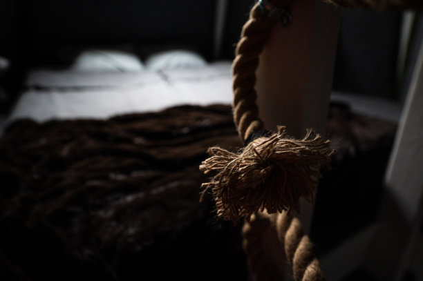 弧形编织麻绳作为木制避暑别墅二楼卧室楼梯栏杆框架的装饰和安全元素。连接到木条的绳子的末端刷。平房二楼的床。图片下载