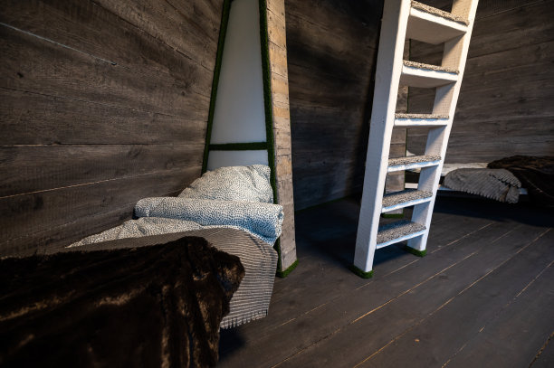 单人床和干净的亚麻布在小木屋的壁龛。金字塔形状的平房避暑别墅。倾斜的围墙，白色的楼梯，灰色的水平木板。非标准框架结构。图片下载