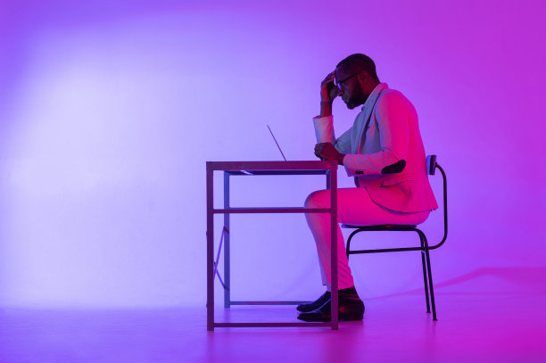 一个男人正坐在书桌前。一个黑人程序员使用笔记本电脑工作。这个人在晚上工作。图片下载