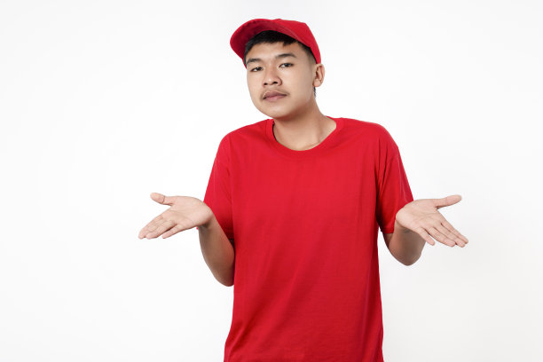 快递员送货概念。穿着红色制服的年轻亚洲送货员微笑着孤立在白色背景上，张开双臂，不知所措，我不知道，没有概念。图片下载
