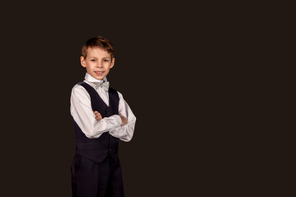 时尚的学生在校服上黑色孤立的背景。小男孩穿着时尚西装，打着领结，学生在工作室里双手交叉看着相机。教育的概念。复制文本空格图片下载