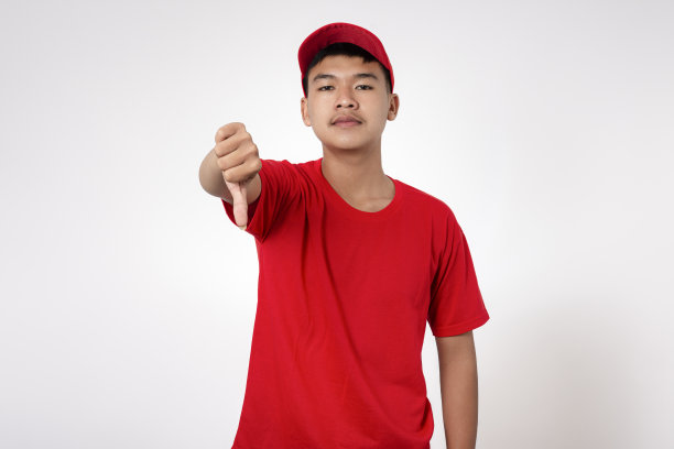 快递员送货概念。微笑的年轻亚洲送货员在红色制服孤立在白色背景做消极的拇指向下手势的手和手指。图片下载