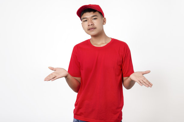 快递员送货概念。穿着红色制服的年轻亚洲送货员微笑着孤立在白色背景上，张开双臂，不知所措，我不知道，没有概念。图片下载