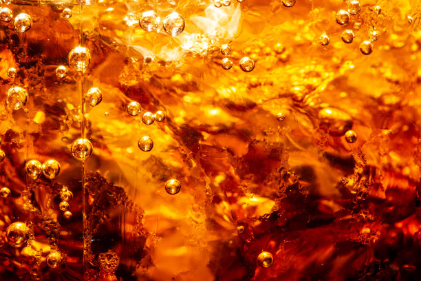 宏观可乐饮料背景，近距离观看冰块在黑暗可乐背景。甜夏季冷饮表面与泡沫和宏观气泡在玻璃墙上。嘶嘶作响或浮到表面的顶部图片下载