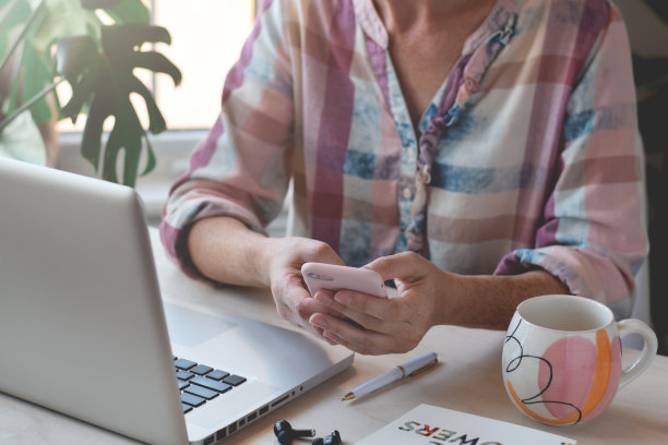 女人的手坐在桌子前的笔记本电脑使用手机图片下载